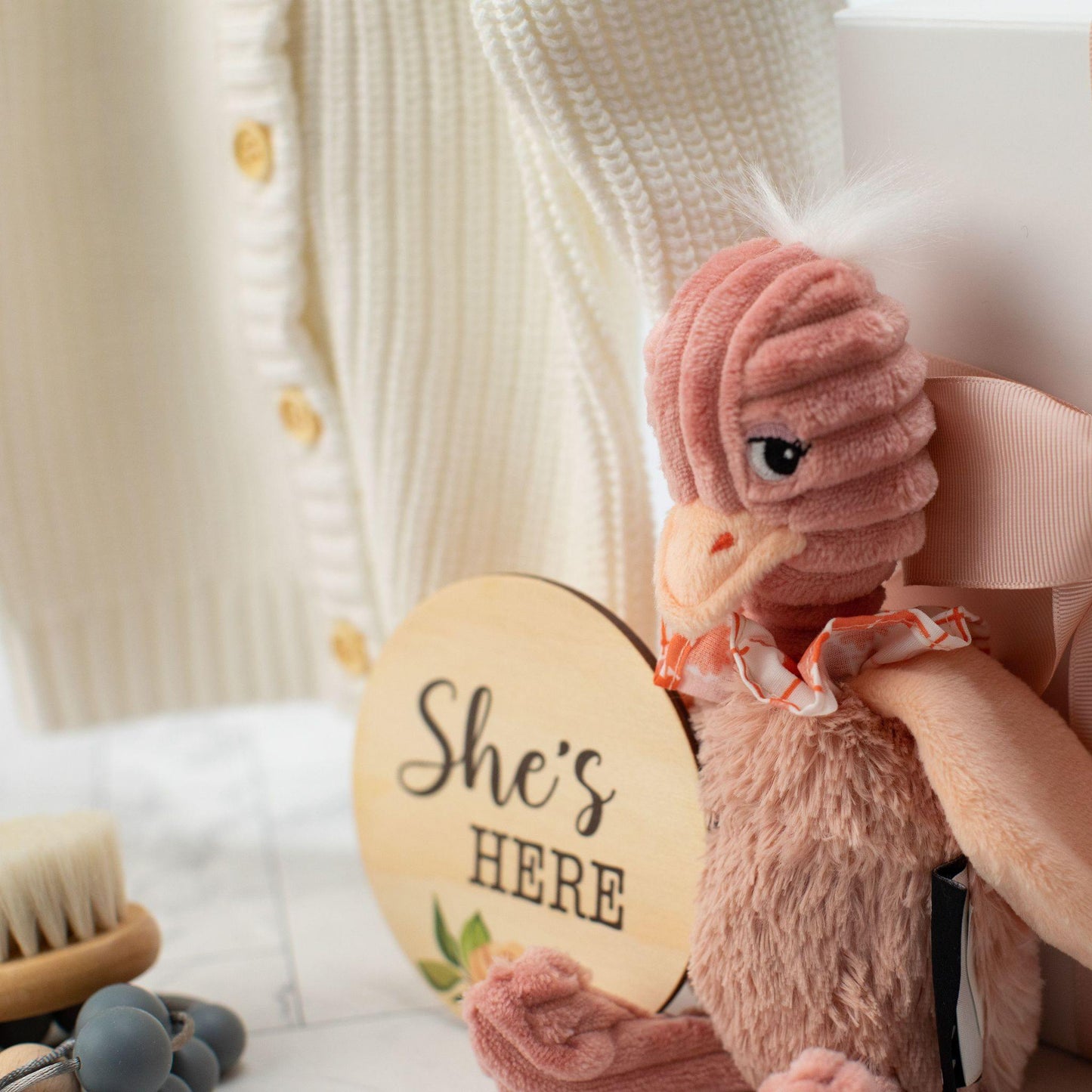 soft pink baby toy next to a white baby cardiagan